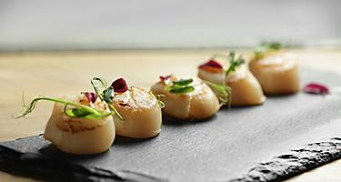 Five scallops on a black plate with garnish