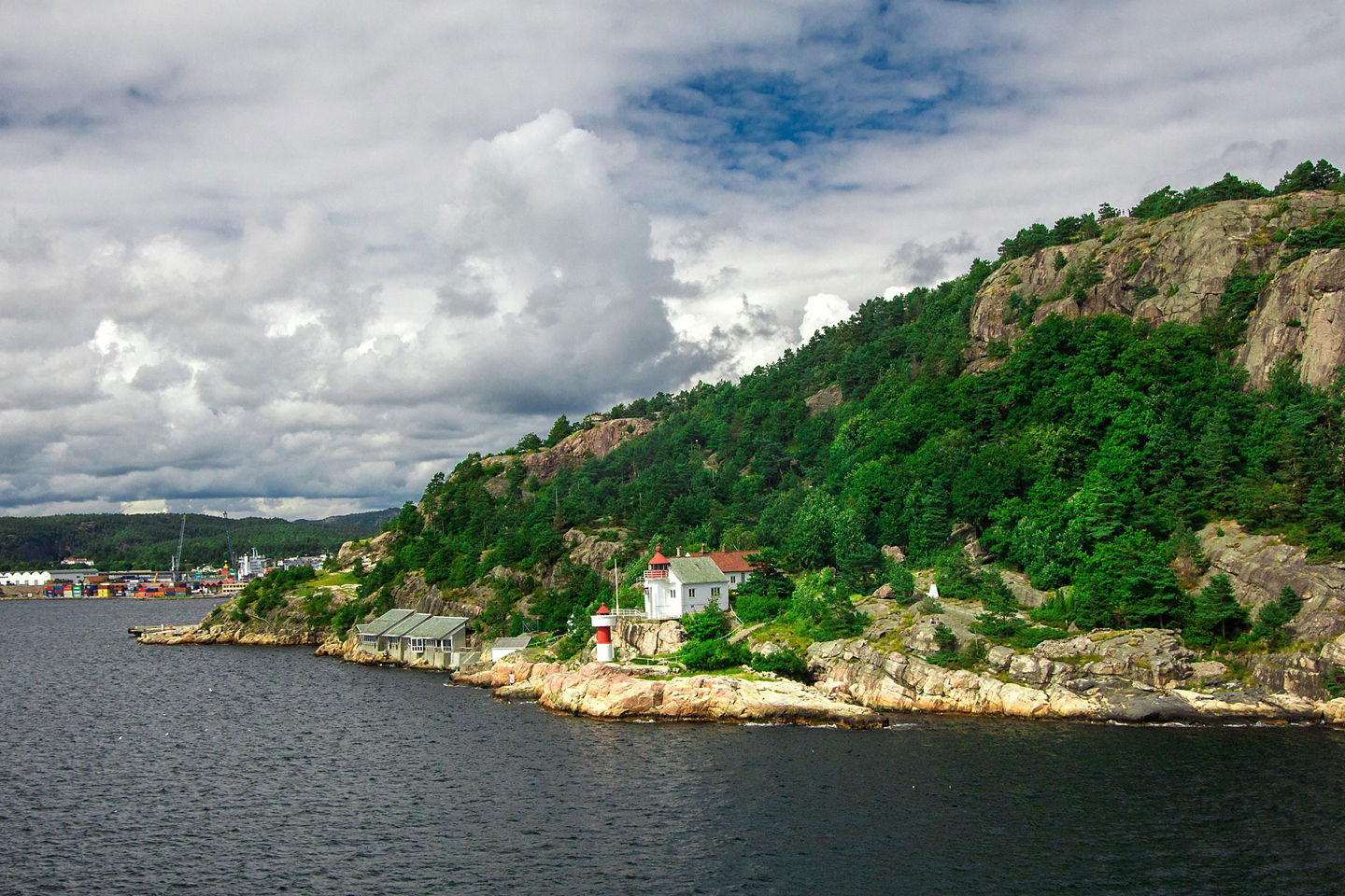 Rocky Kristiansand shore rises toward forested mountains. - Kristiansand, Norway
