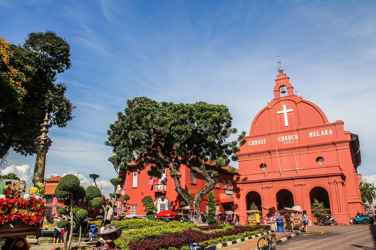 A historic red church stands beside a quiet canal, framed by trees and old brick buildings. - Malacca, Malaysia