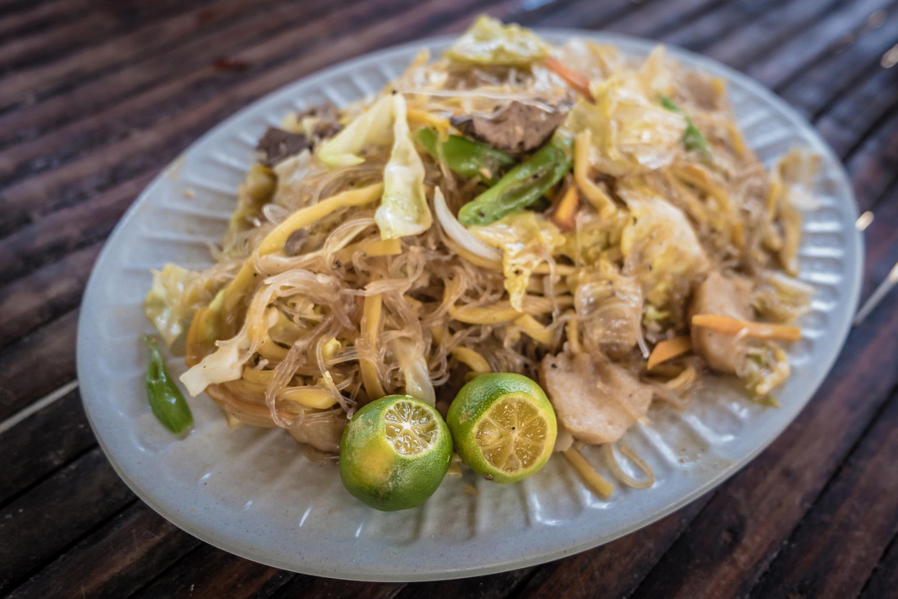 Traditional food in the Philippines with noodles, vegetables, and lime served on the side