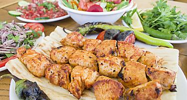 Multiple chicken shish kebobs with a bowl of salad on the side