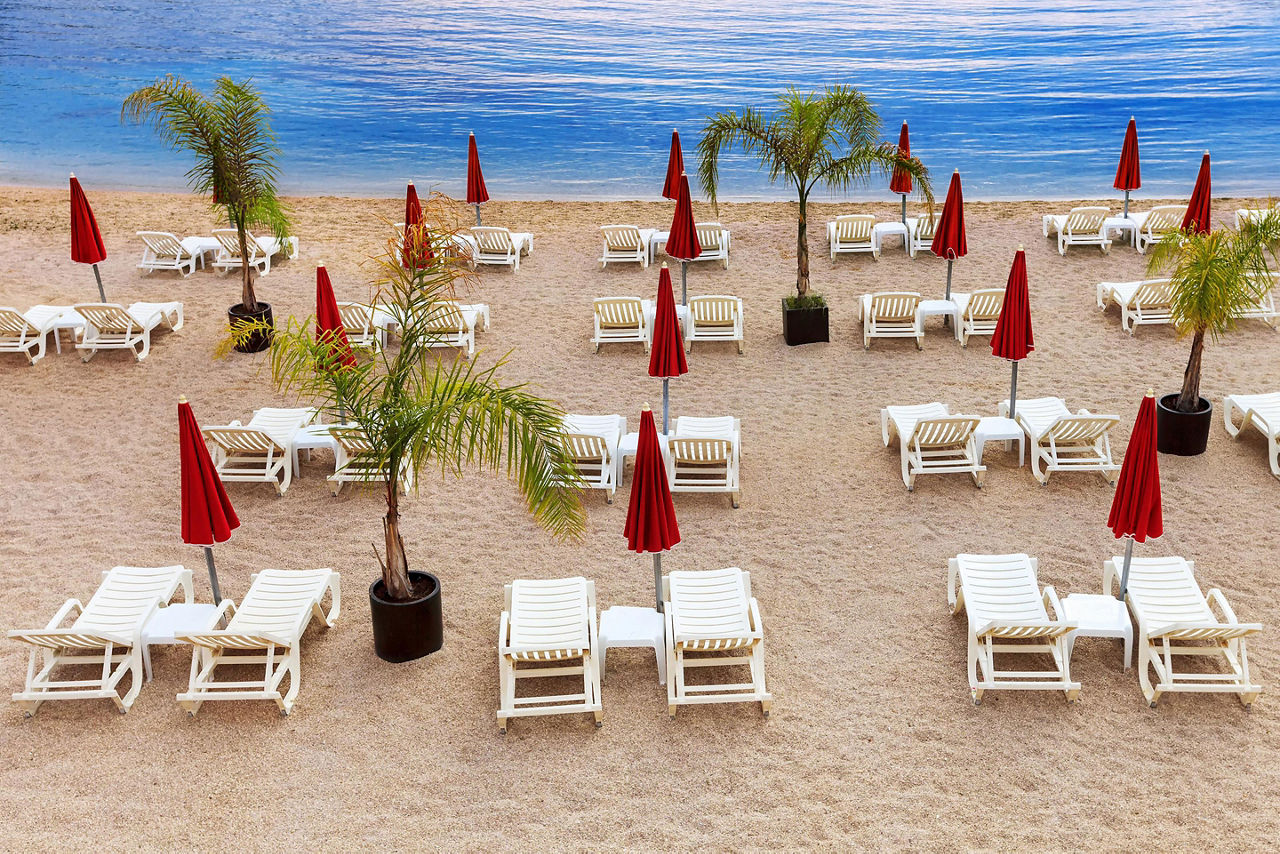Stylish mediterranean beach with white sunbeds and red umbrellas in Monte Carlo, Monaco