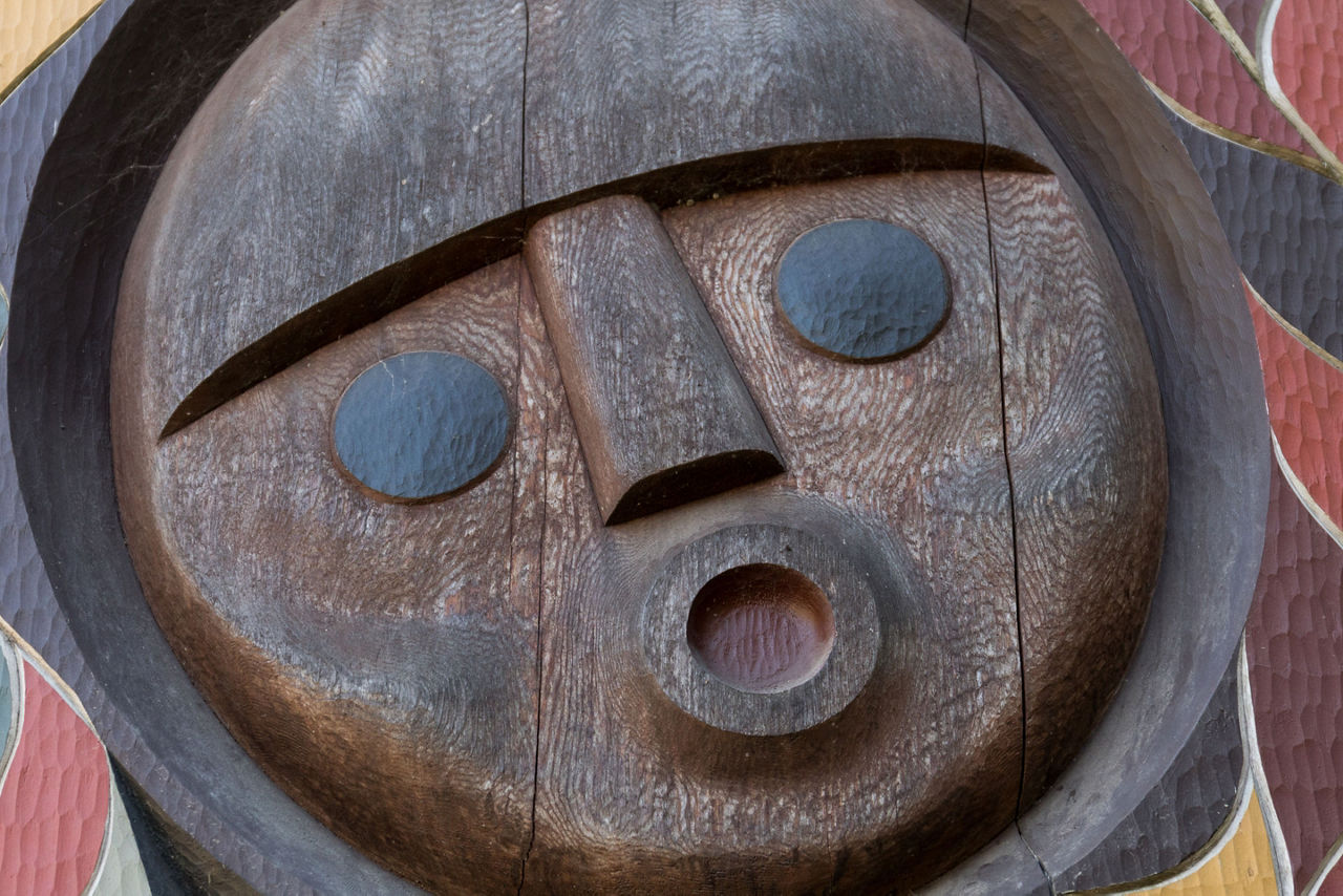 A face carved in wood surrounded by colorful designs
