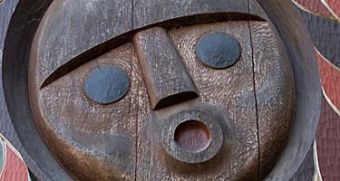 A face carved in wood surrounded by colorful designs