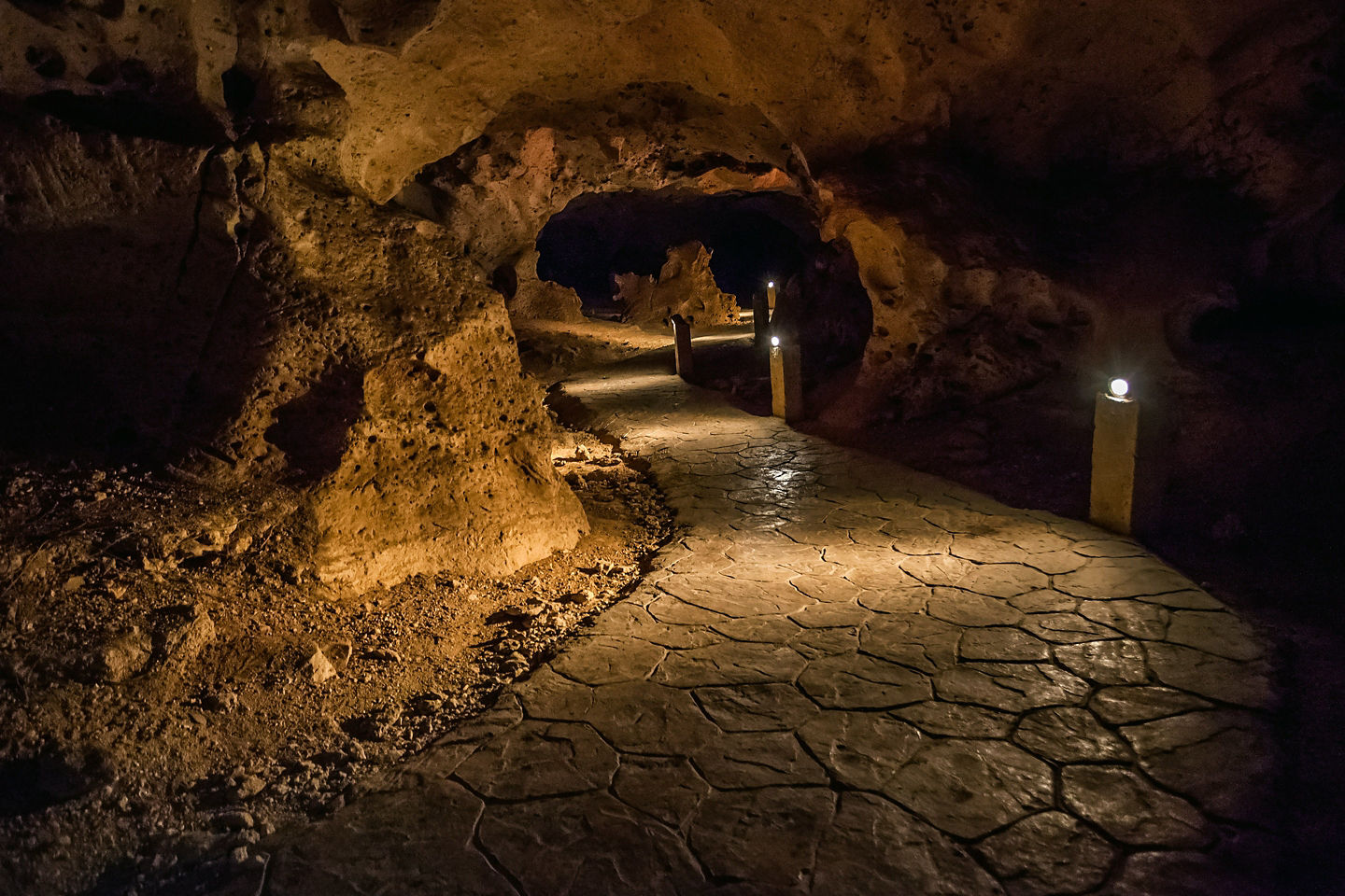 A stone pathway winds through a cool grotto, framed by textured limestone walls and soft light. - Ocho Rios, Jamaica