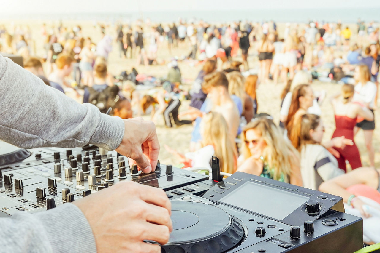 Close up of DJ's hand playing music at turntable at beach party festival - Crowd people dancing and having fun in club outdoor