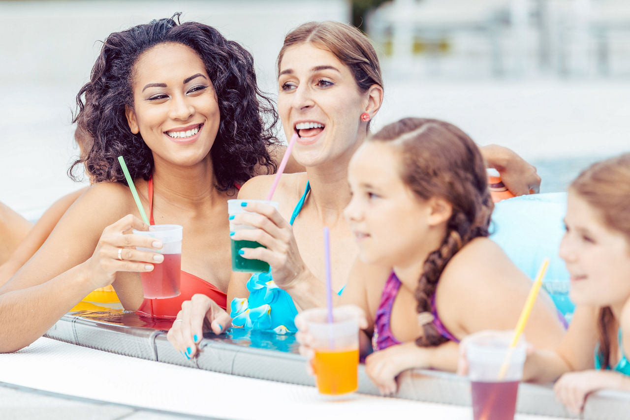 Smiling family with glasses of juice resting in rooftop swimming pool. Orlando, Florida.