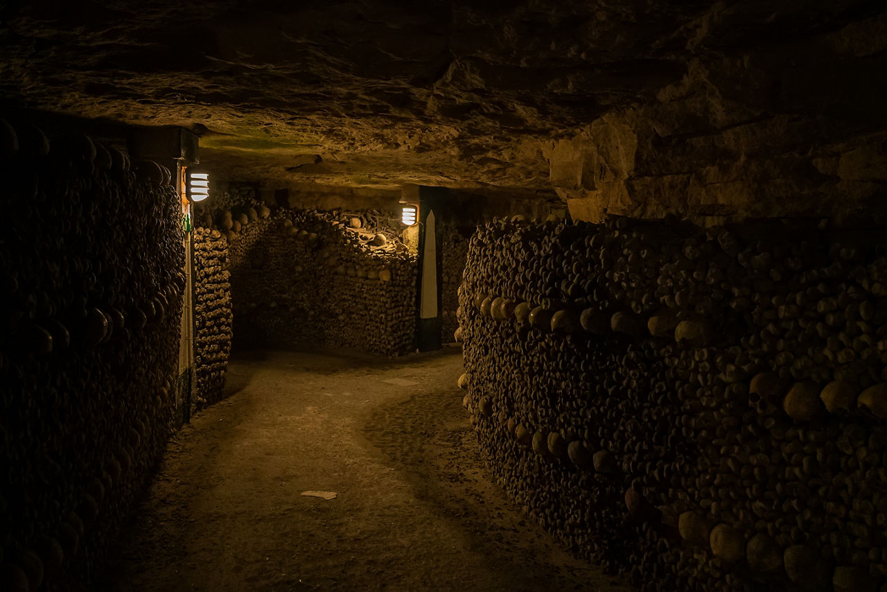 Pathway in catacombs. Old skulls and bones form walls. Grim lighting. Underground cemetery.