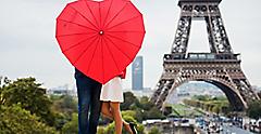 Couple visiting the Eiffel Tower standing with a red heart-shaped umbrella in Paris. Europe.