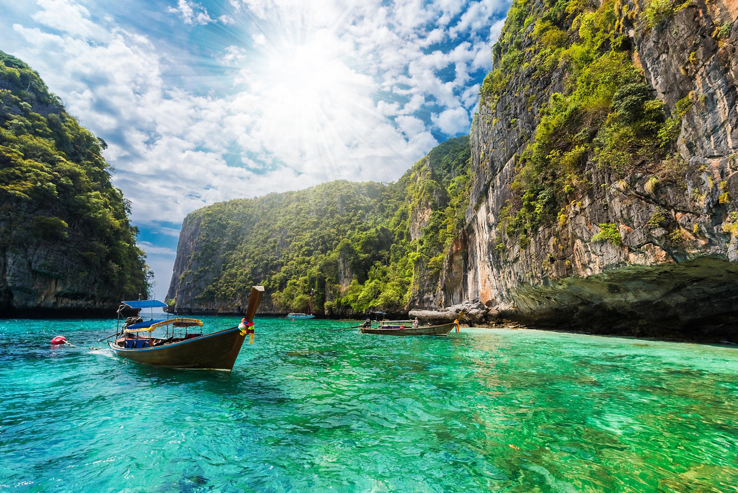 A small boat glides across Phuket’s calm blue water beneath rugged green coastal cliffs. - Phi Phi Islands, Thailand