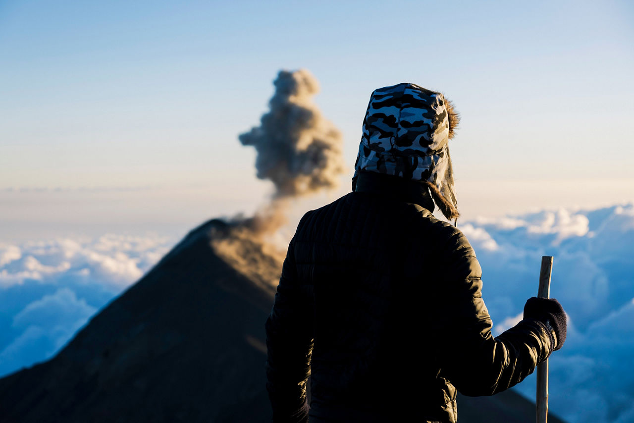 Hiker on top of Acatenango volcano watching Fuego volcano eruption
