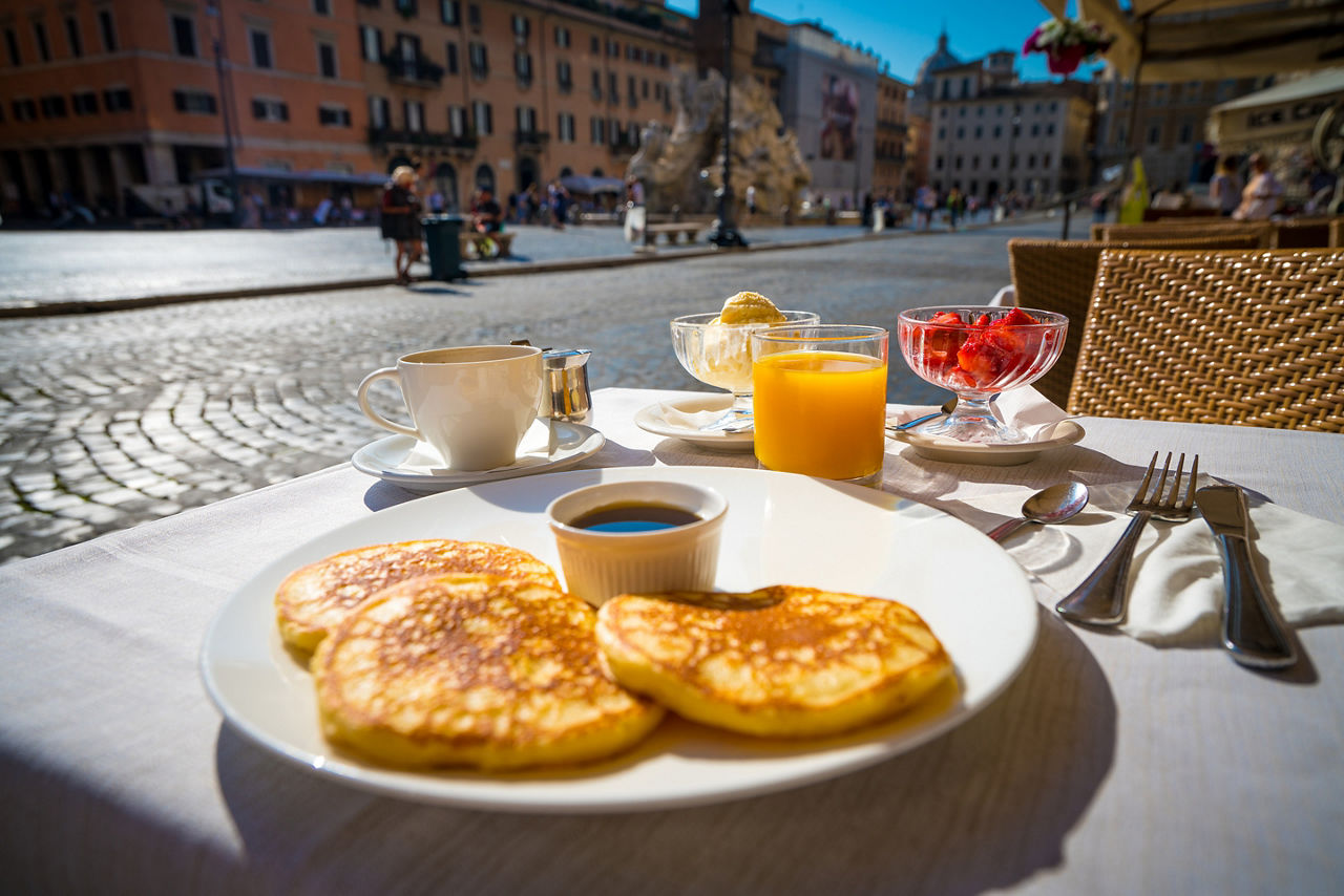 Italian breakfast including pancakes fruits and drinks on the background of Piazza Navona in Rome,Italy