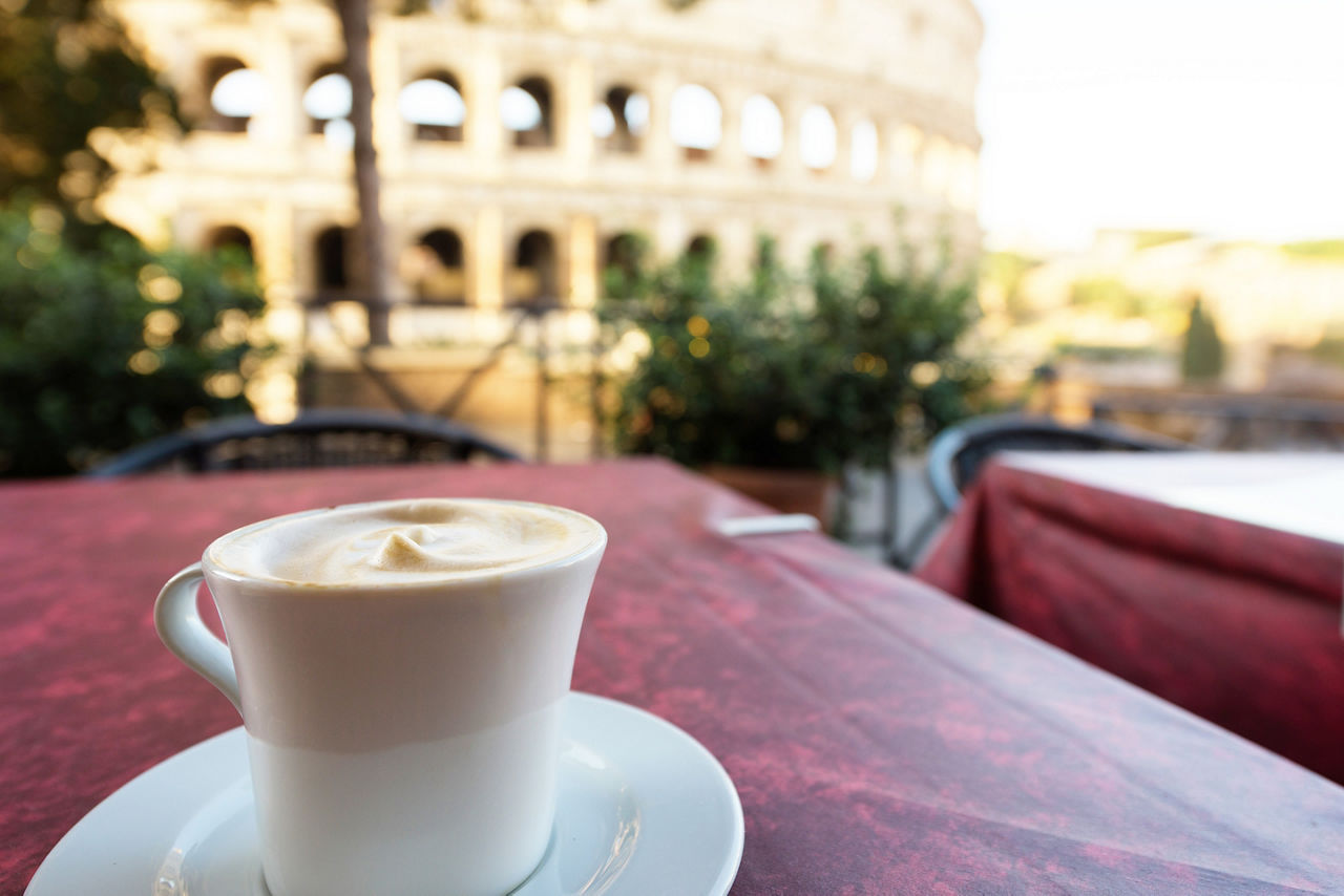 Italian cappuccino coffee cup on a table, with roman coliseum in background, at sunrise in Rome, Italy.