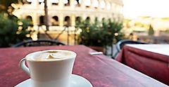 Italian cappuccino coffee cup on a table, with roman coliseum in background, at sunrise in Rome, Italy.