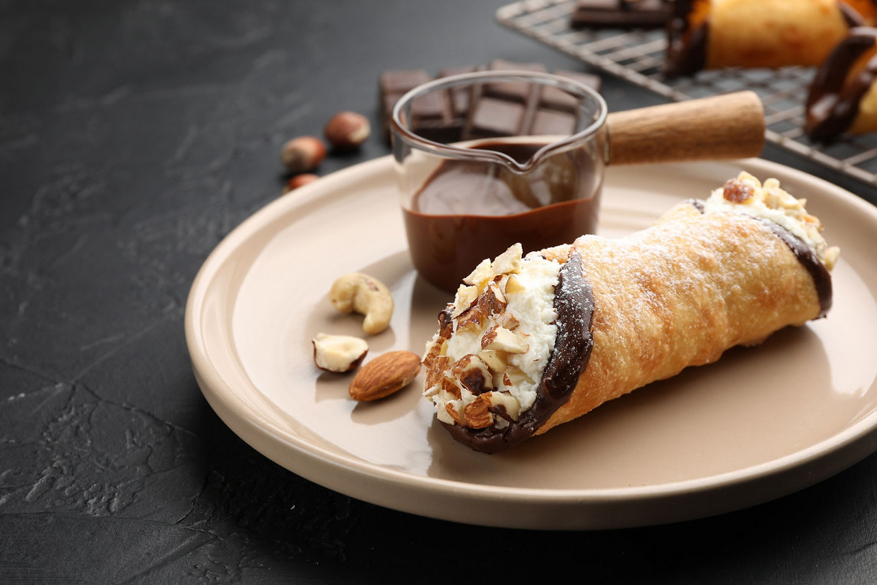 Delicious canoli with cheese, chocolate and almonds on black table, closeup