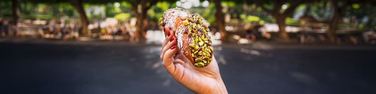 Female hand holding a pistachio cannoli in front of a park
