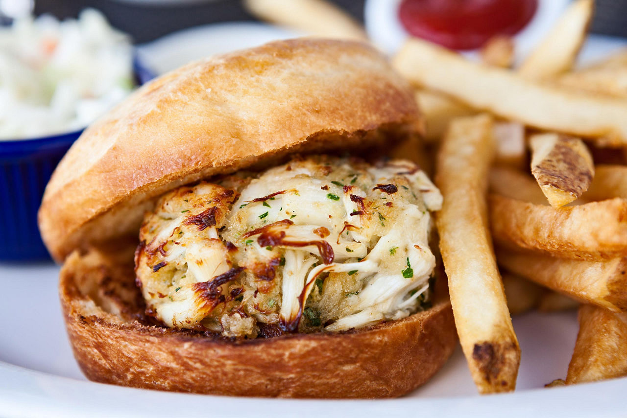 A crab cake sandwich with a side of french fries and cole slaw