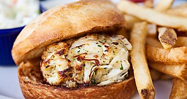 A crab cake sandwich with a side of french fries and cole slaw
