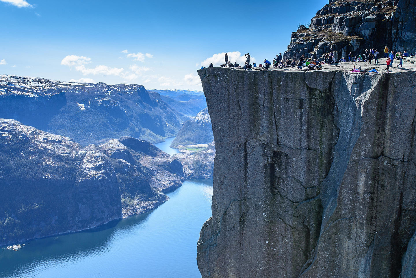 Hikers stand atop Preikestolen overlooking a vast blue fjord. - Stavanger, Norway