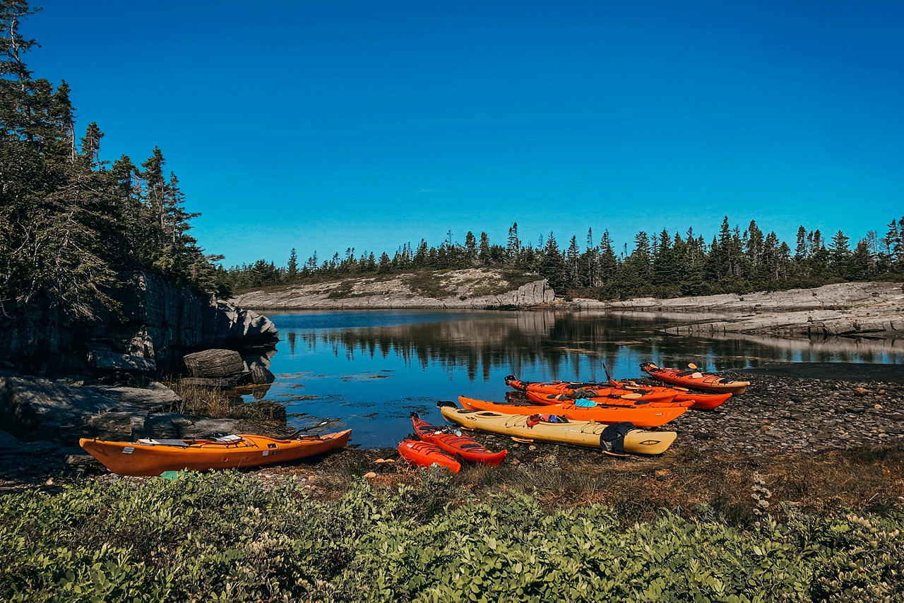 Beautiful and colorful image of several rental kayaks resting on the Atlantic Ocean shoreline. Taken on a seal watching kayak excursion in Blue Rocks, Nova Scotia, Canada.