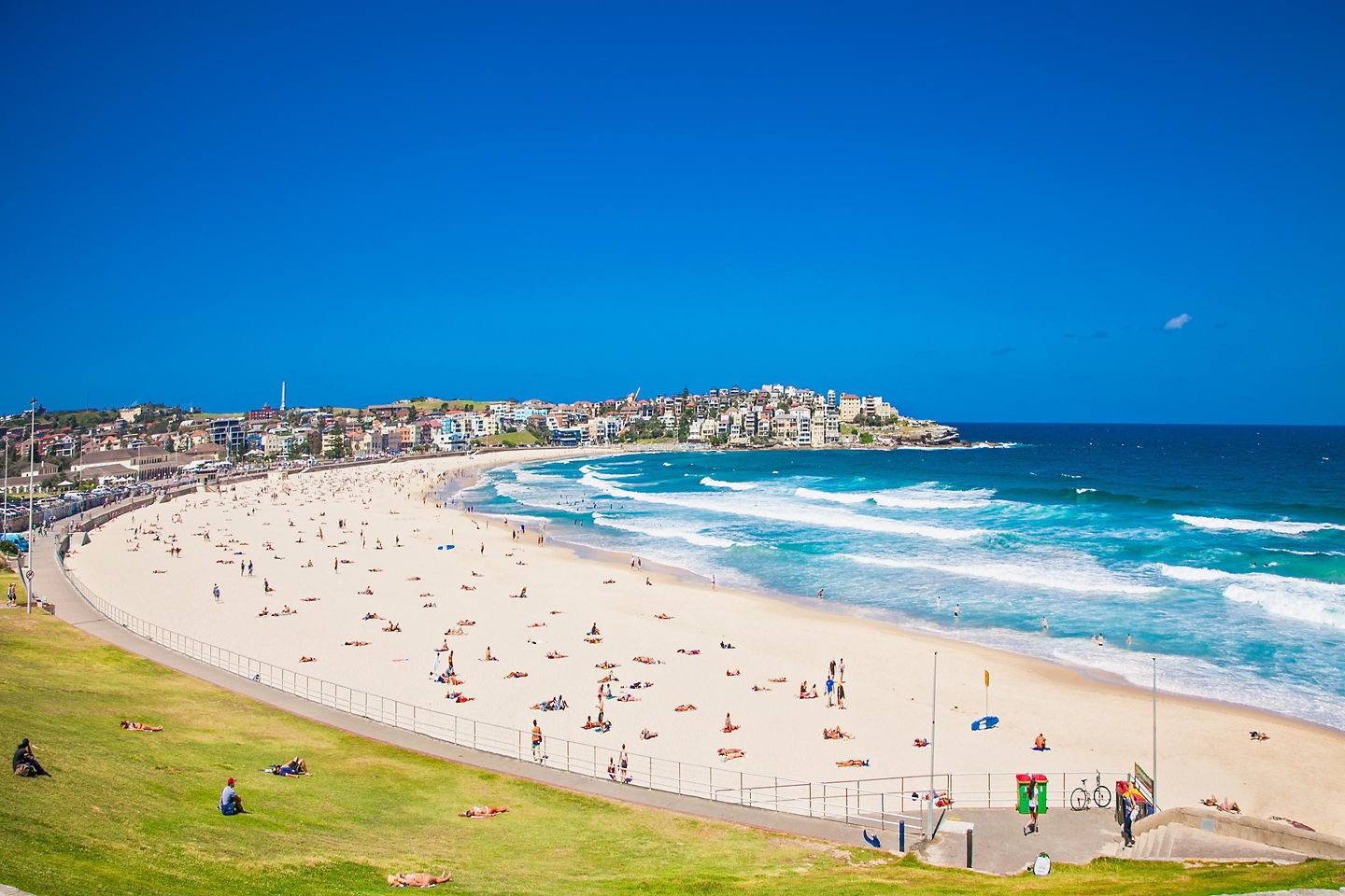 People relaxing on Bondi Beach with waves and bright blue sky.