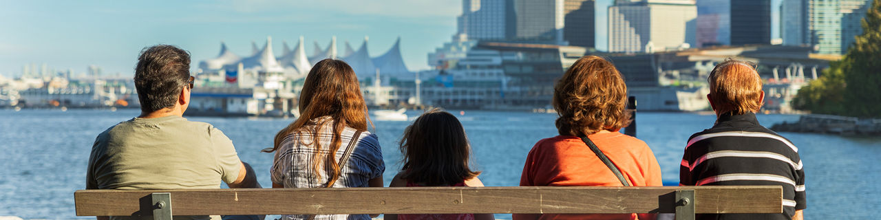 Family sitting on a bench at Stanley park watching the Vancouver Skyline. 