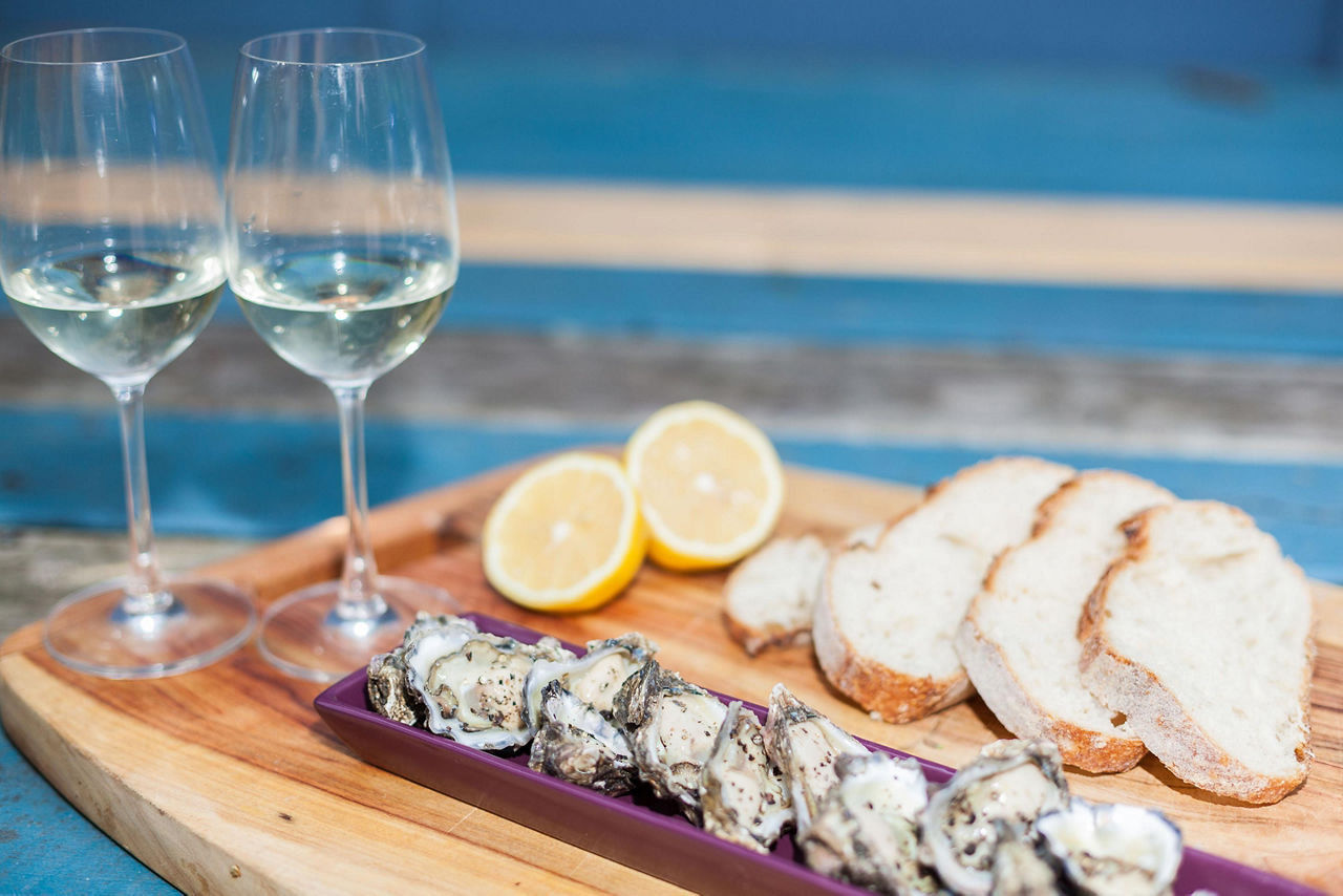 A platter with oysters with two glasses of wine, bread and a sliced lemon