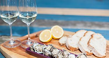 A platter with oysters with two glasses of wine, bread and a sliced lemon