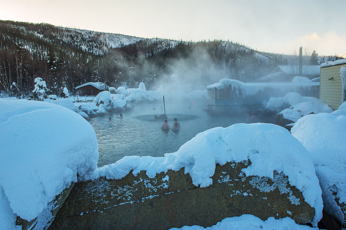 Snowy mountains surround Chena Hot Springs, with warm geothermal pools steaming in the cold air. - Chena Hot Springs, Alaska