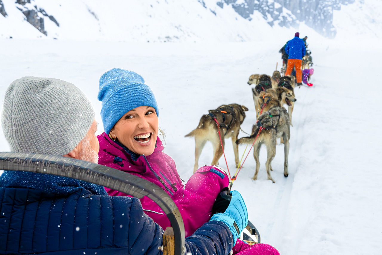 Couple rides on a dog sled pulled by a team of dogs