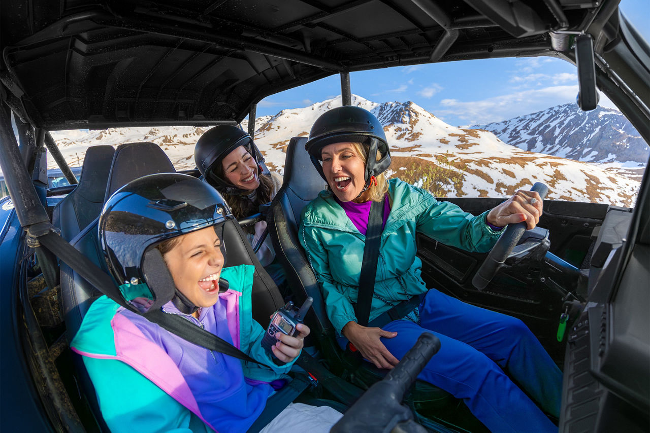 Three people ride in an off-road vehicle in snowy mountains in Sitka Hatcher Pass Alaska