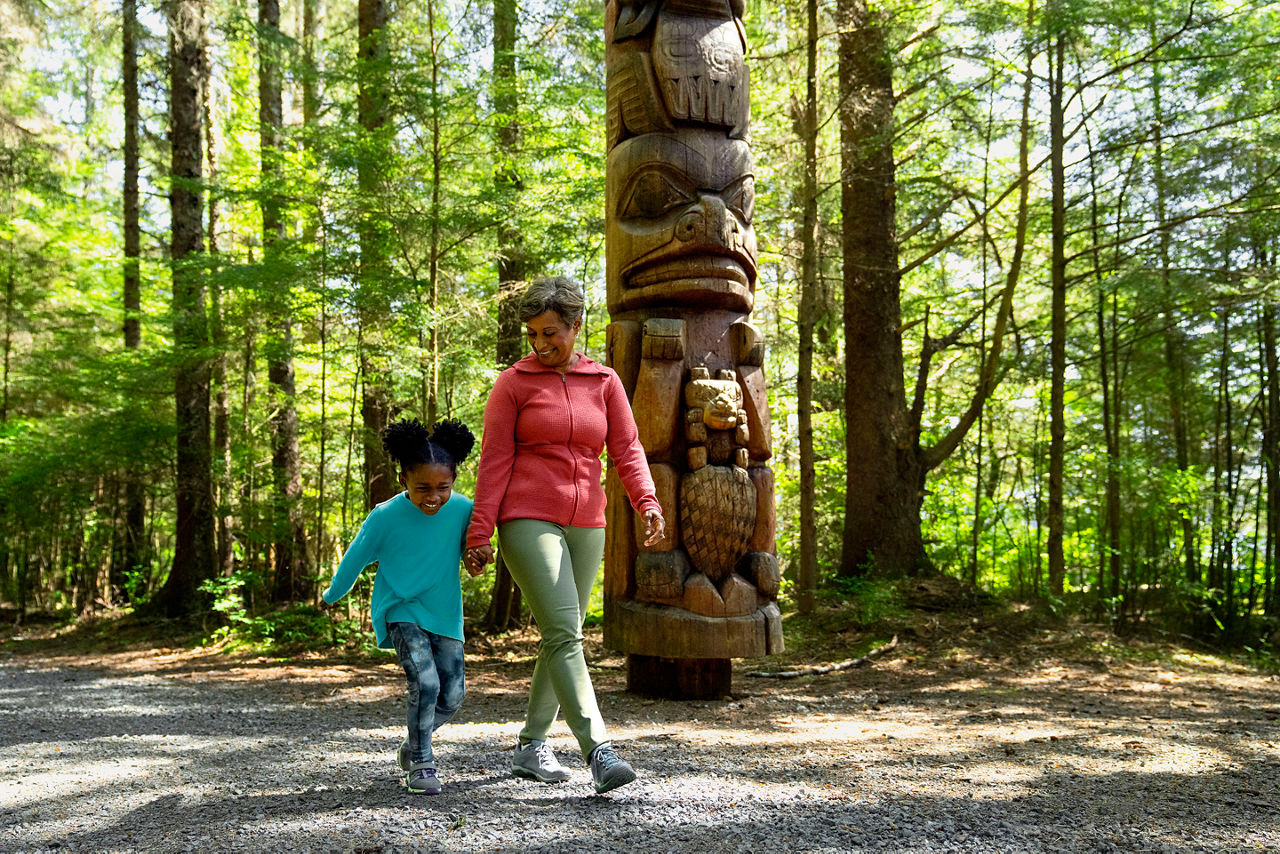 Woman and little girl walking past a totem in Alaska