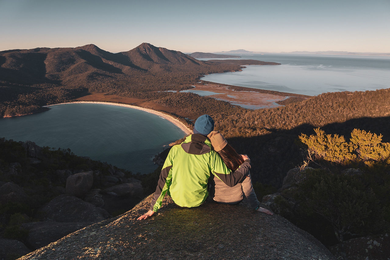 Couple watching sunrise at the peak of Mount Amos with Wineglass Bay at the background