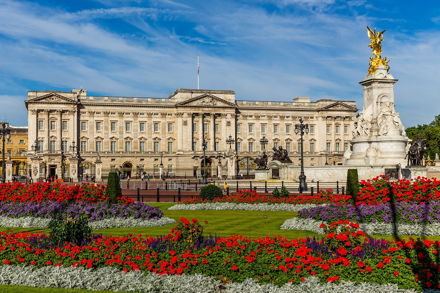 Buckingham Palace stands behind bright red flowers. - London, England