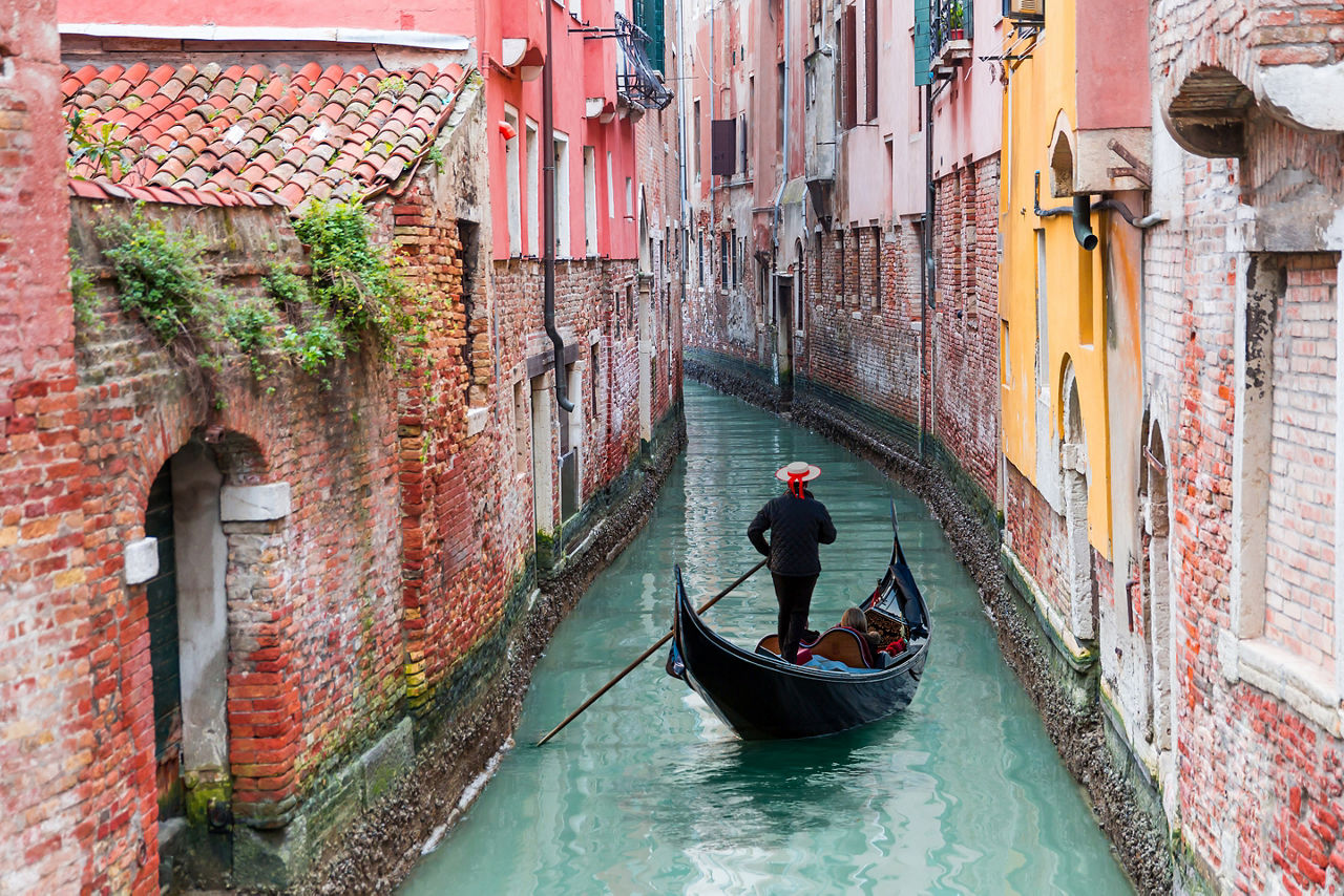 Gondolier punting gondola through green canal waters of Venice. Italy.