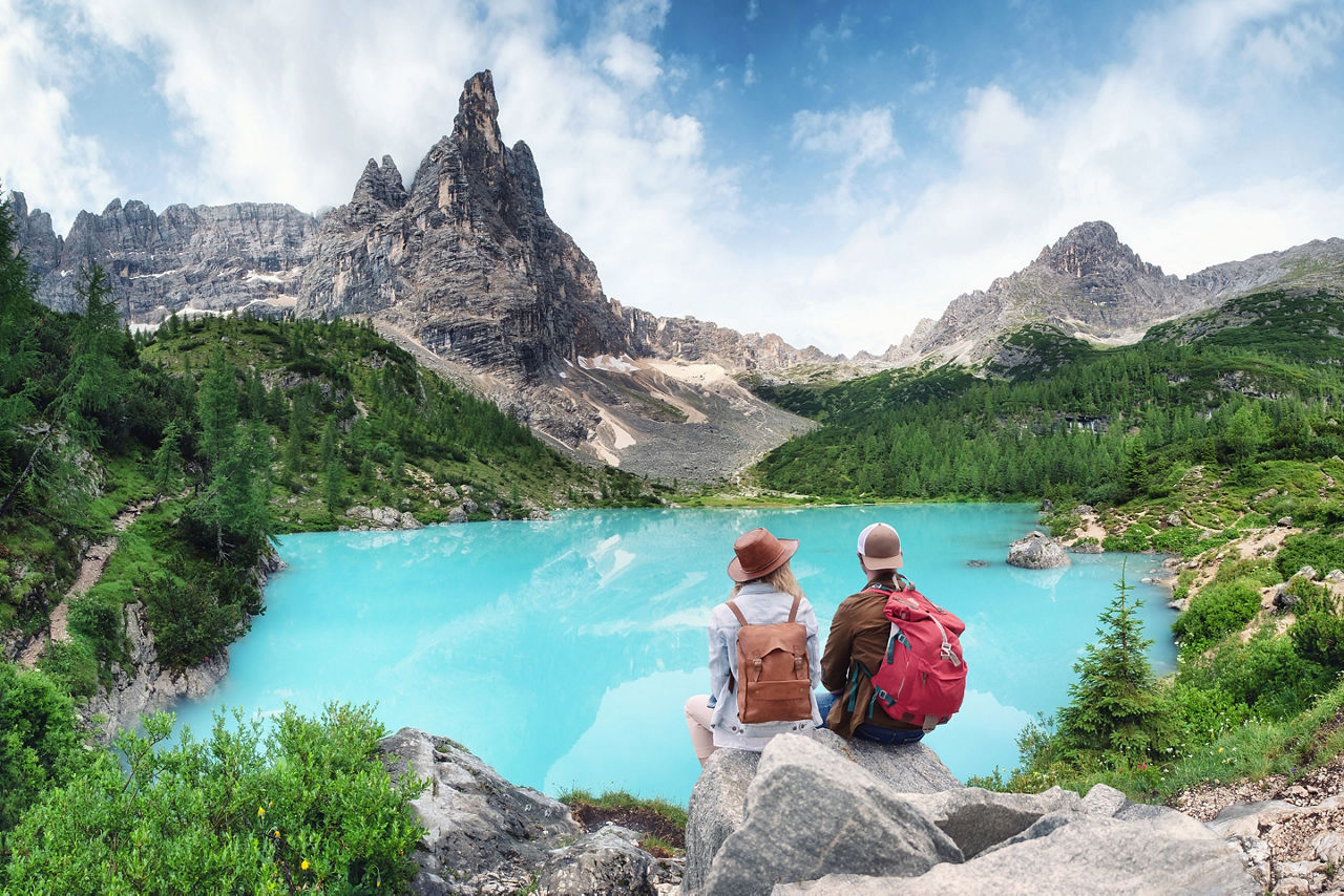 Travelers couple look at the mountain lake. Travel and active life concept with team. Adventure and travel in the mountains region in Dolomite alps, Italy