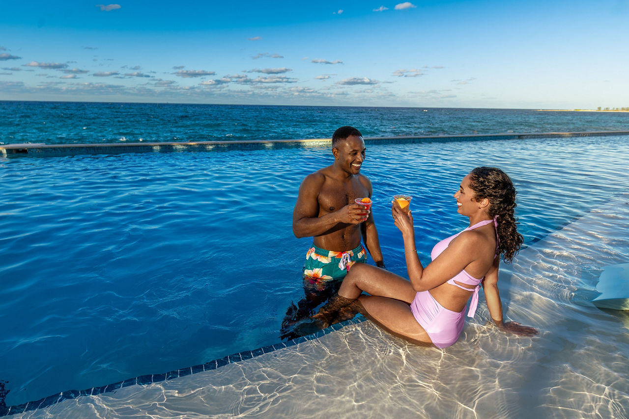 Couple drinking and lounging at the pool at Chill Beach at Royal Beach Club Paradise Island, fun, romance,
