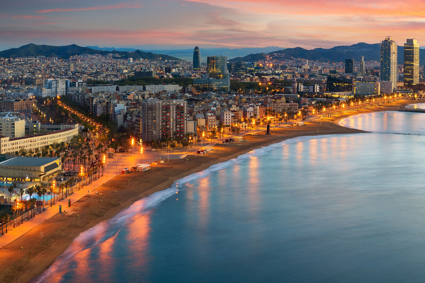 Barcelona’s shoreline glows at sunrise, with the city stretching along the calm Mediterranean coast. - Barcelona, Spain