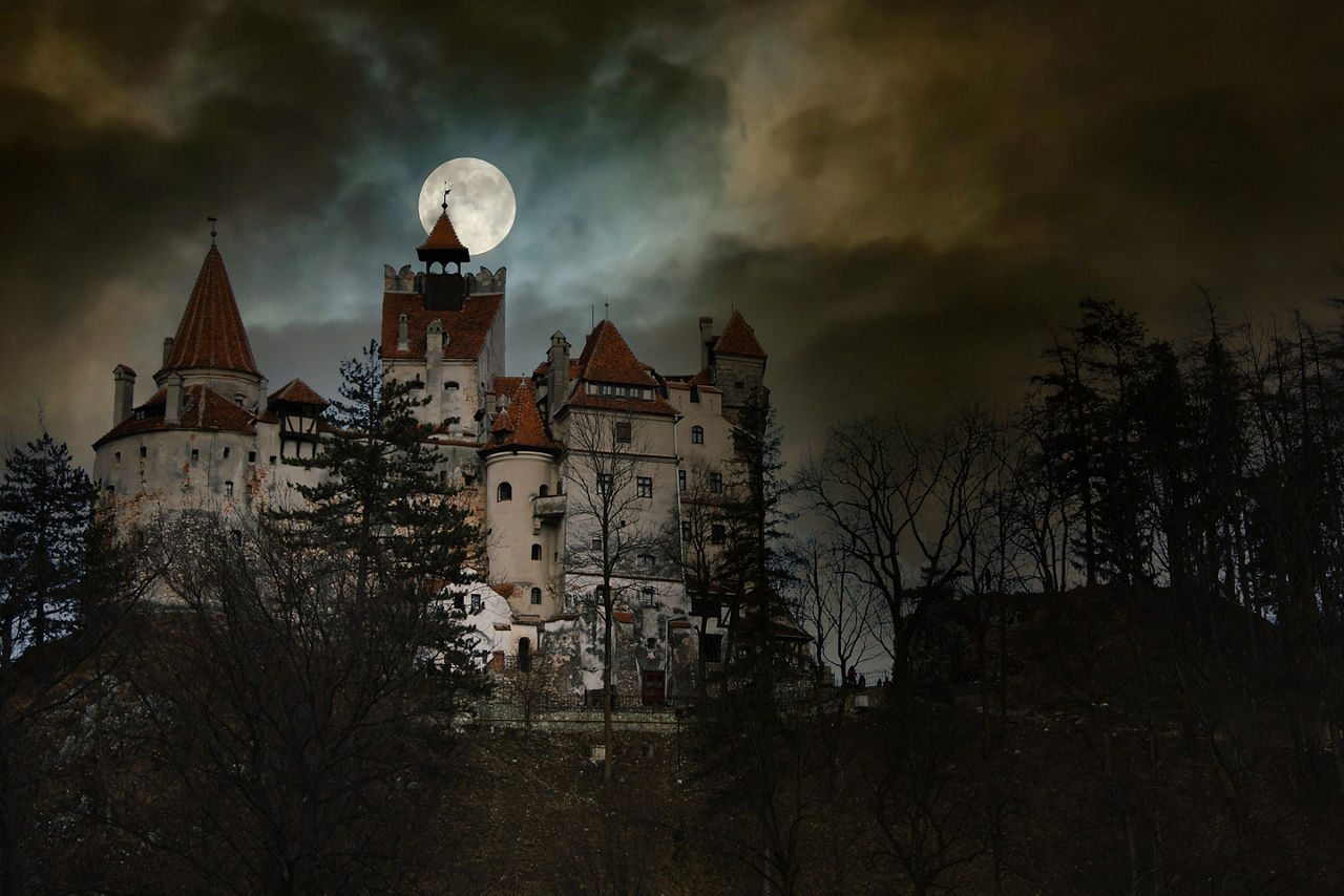 Moon in the clouds over Bran Castle, Transylvania, Romania. Medieval building, Dracula's Castle. Mystical night landscape.