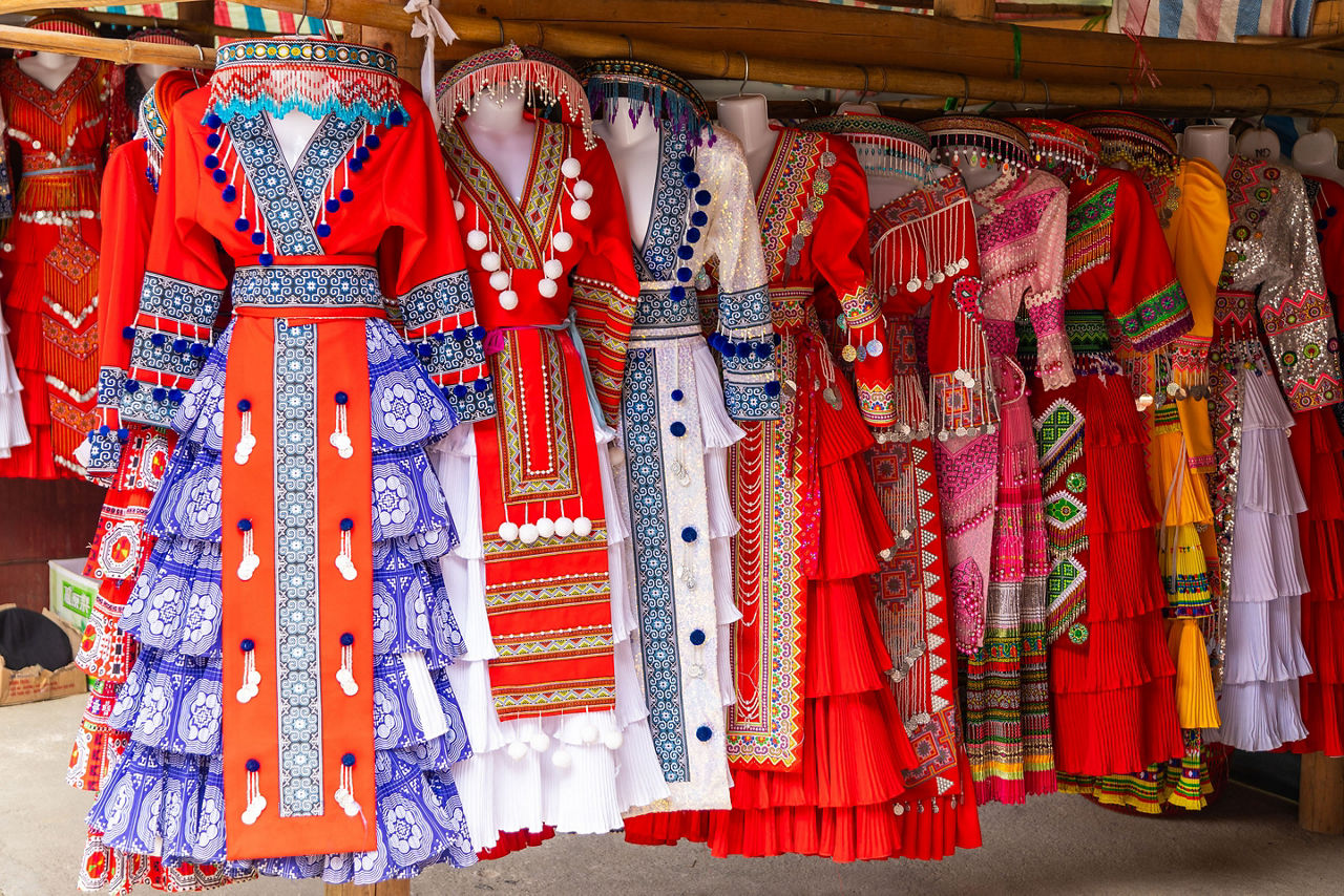 Traditional Vietnamese garments with colorful embroidery and handcrafted details are displayed for sale at a local market stall.