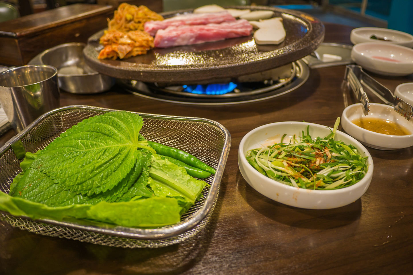 Korean black pork barbecue cooks on a tabletop grill, surrounded by colorful traditional side dishes. - Jeju, South Korea