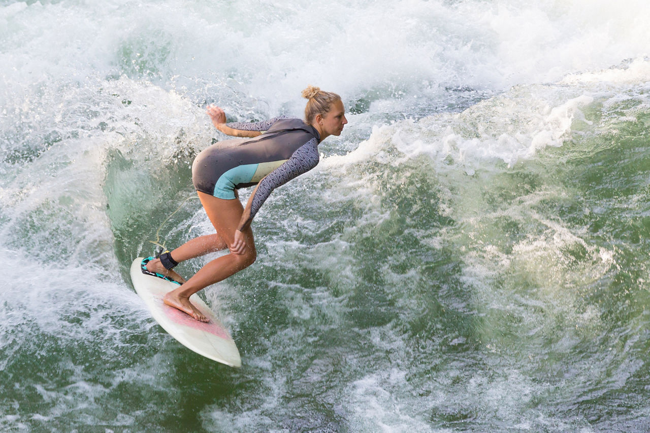 Atractive sporty girl in neoprene shorty surfing on famous artificial river wave in Englischer garten, Munich, Germany