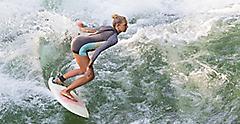 Atractive sporty girl in neoprene shorty surfing on famous artificial river wave in Englischer garten, Munich, Germany
