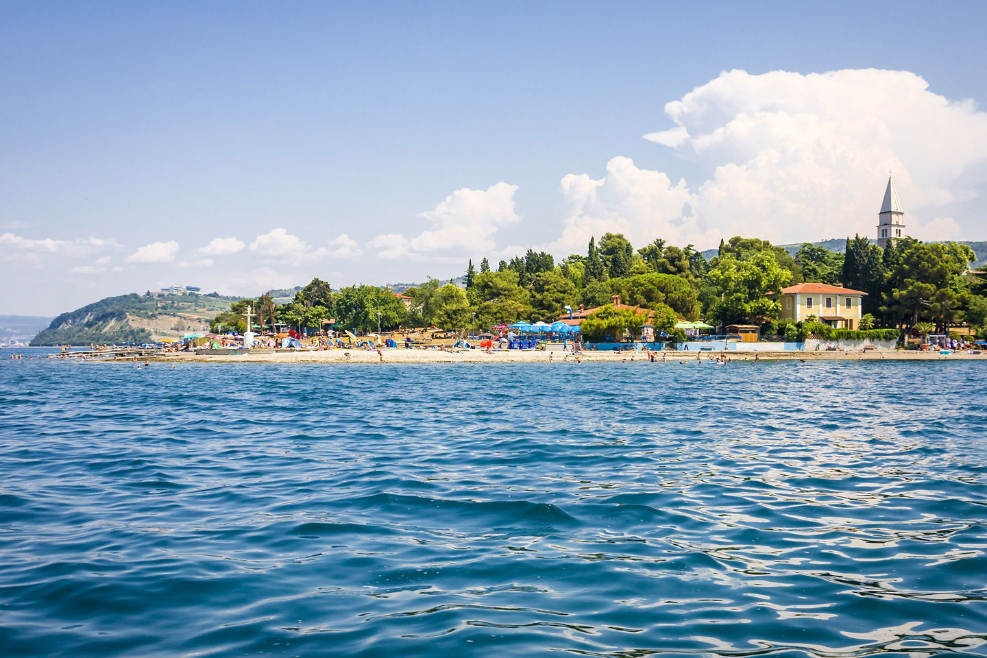 Koper’s coastline curves along the Adriatic, framed by blue water and rolling green hills. - Koper, Slovenia