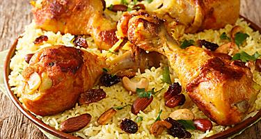 Homemade Arabic spiced rice and chicken topped with nuts, raisins closeup in the plate on the table. 