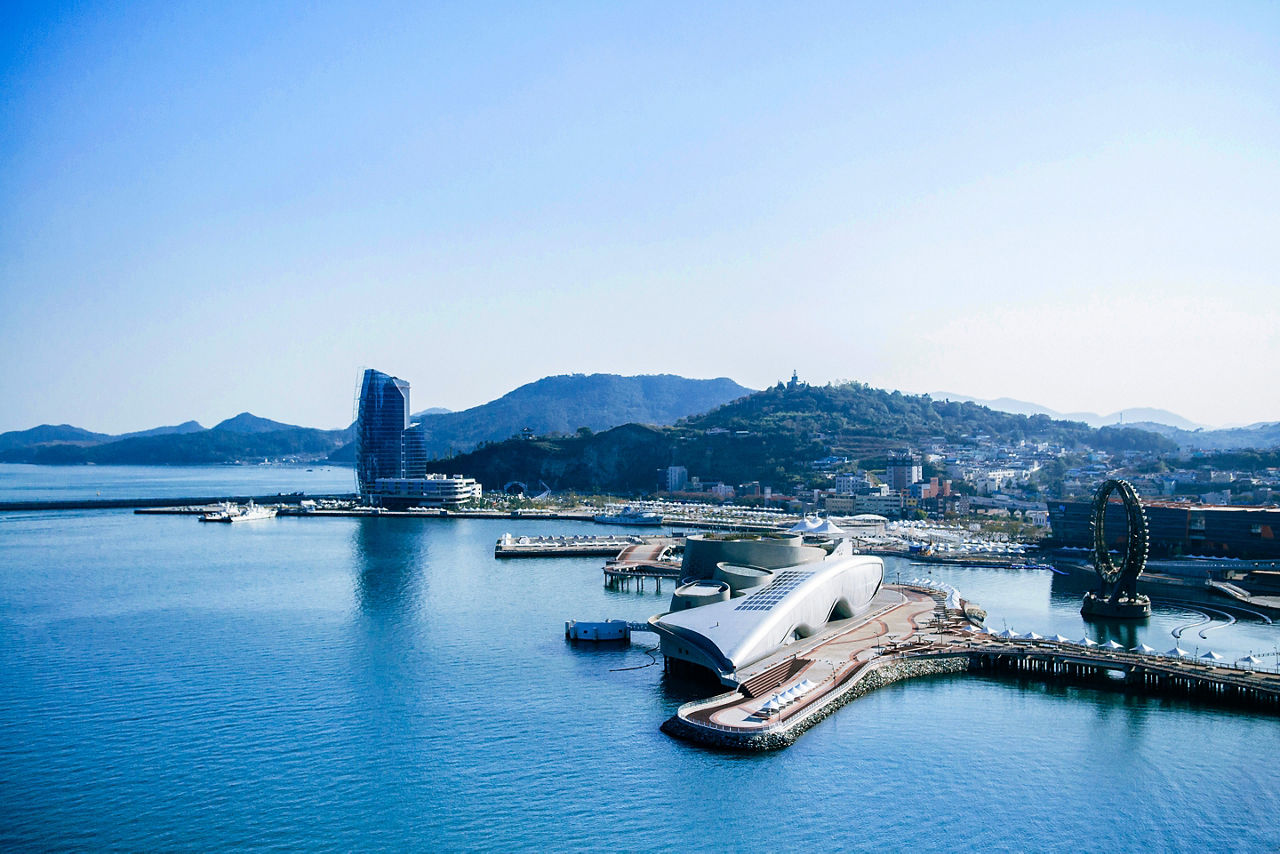 Yeosu, South Korea - Yeosu expo port ferris wheel and modern exhibition halls with mountain in background.