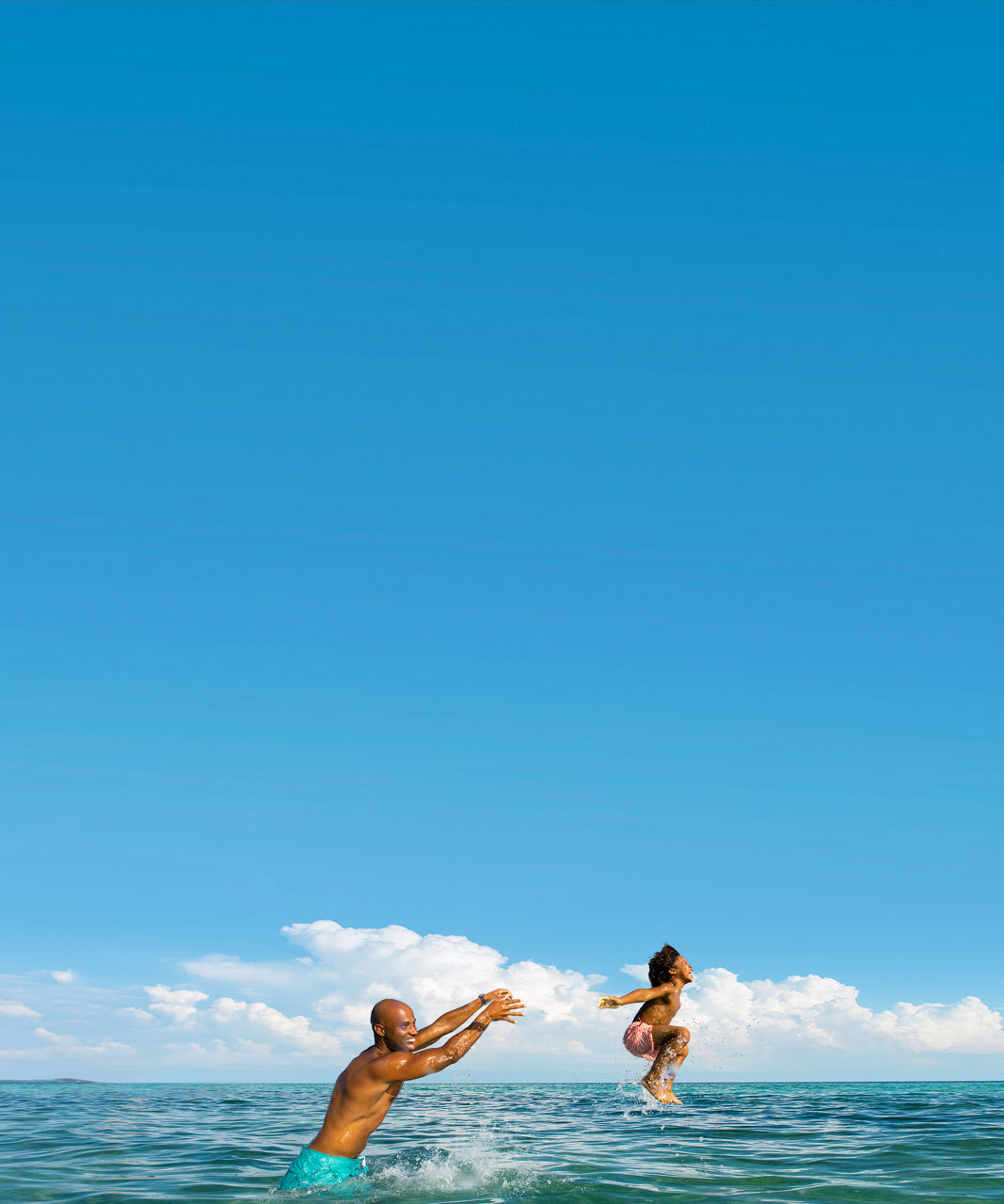 Man laughing in the ocean throwing kid on the air