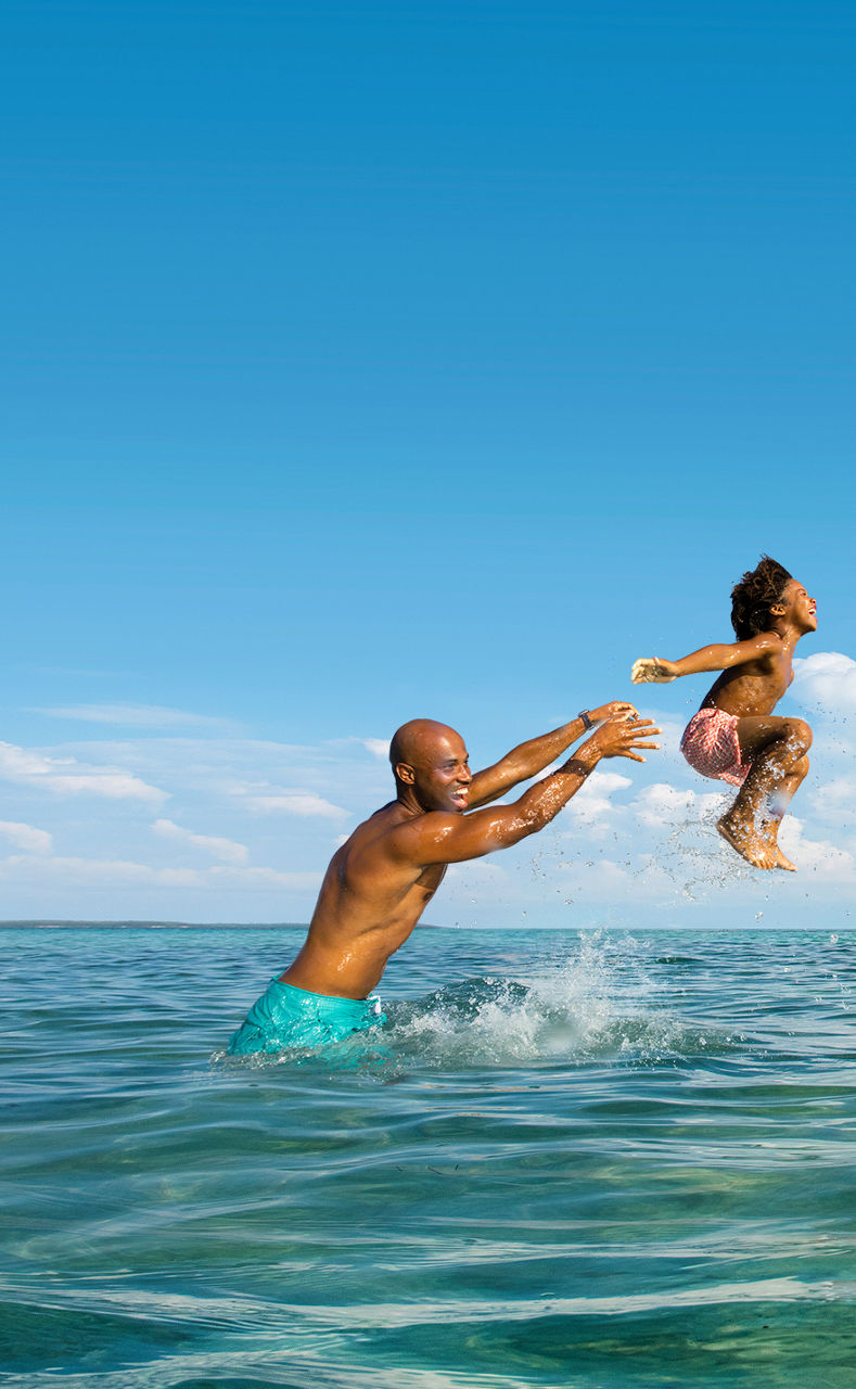 Man laughing in the ocean throwing kid on the air