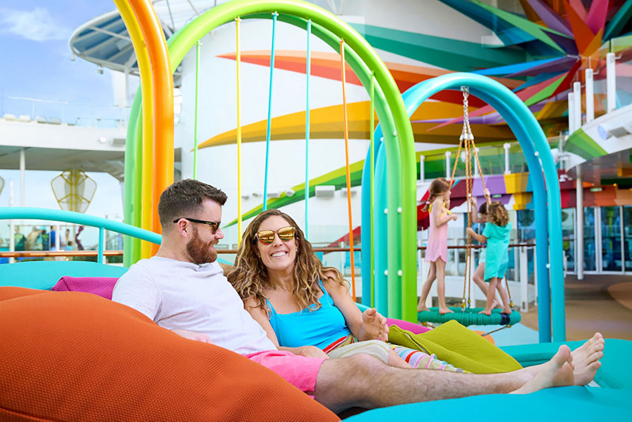 Couple relaxing in Hammock at Chill Island with kids playing in background Icon of the Seas