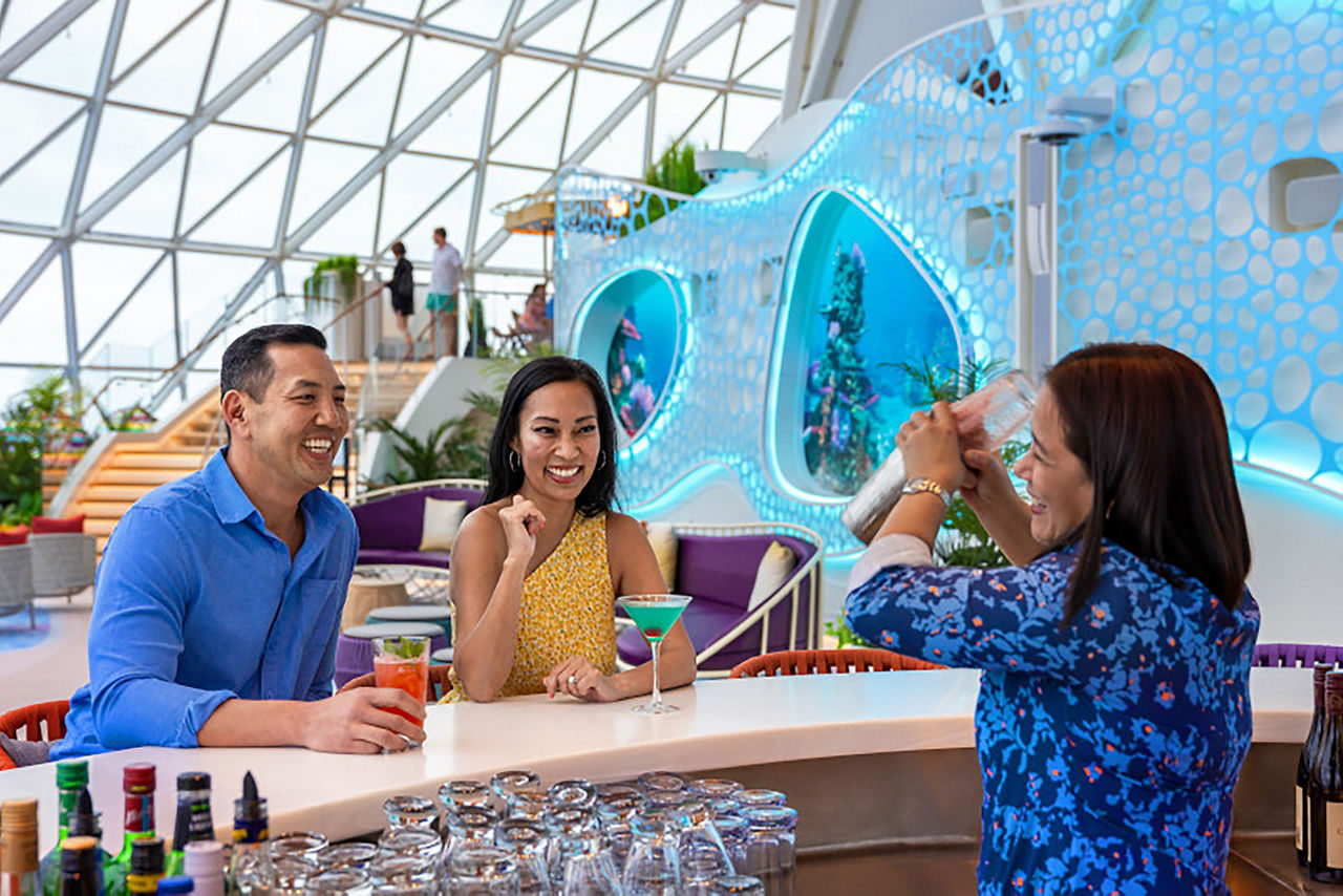 Couple sitting at Overlook Bar on Icon of the Seas while bartender makes a drink, cocktails, fun, relaxing,
